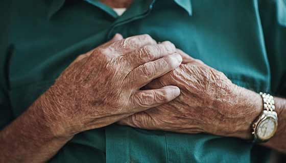 A senior man rests his hands on his chest.
