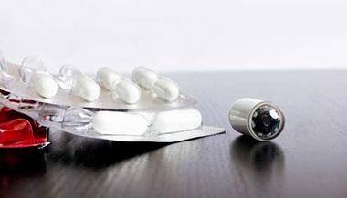 Endoscopy capsule next to regular pills on a table.