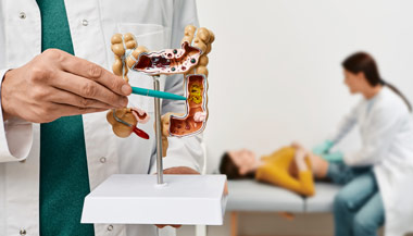 Doctor pointing to intestines model while another doctor examines a patient in the background