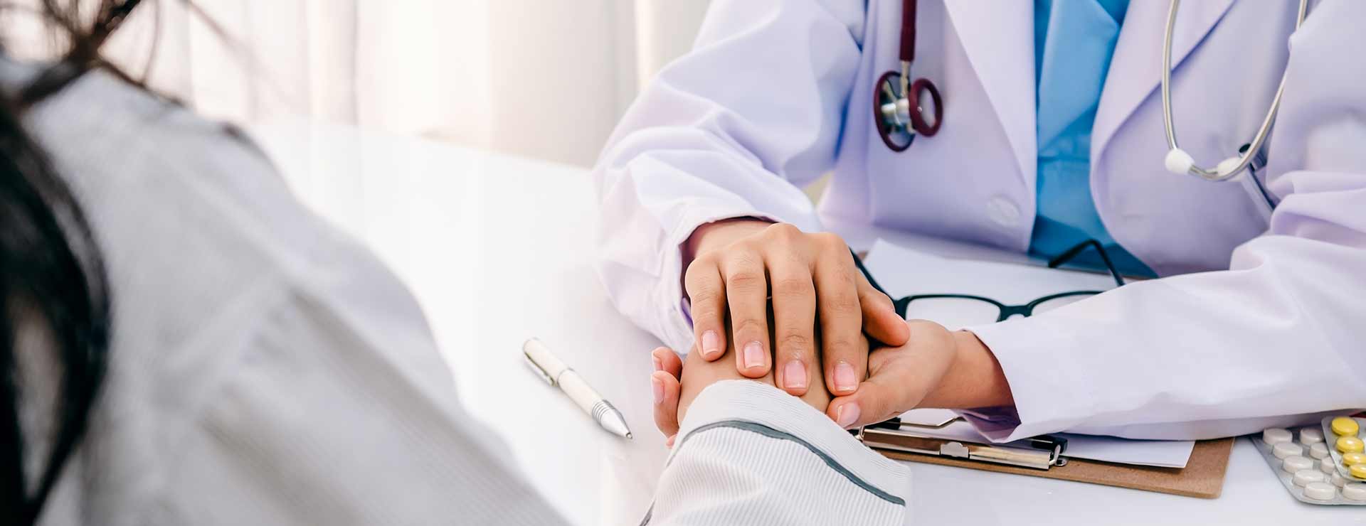 A doctor holds a patient's hand during a consultation.