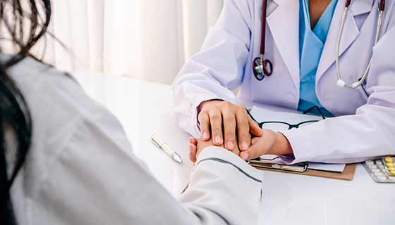 A doctor holds a patient's hand during a consultation.