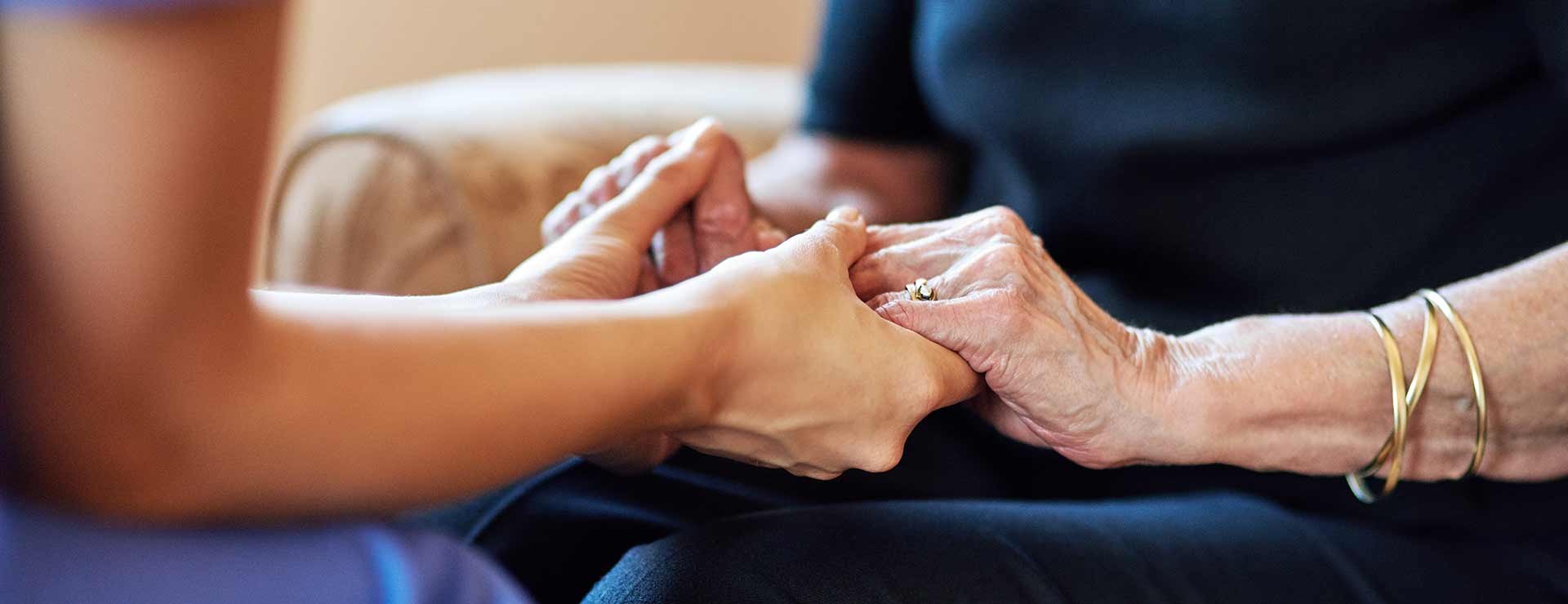 An older woman and younger woman hold hands in a display of loving support.