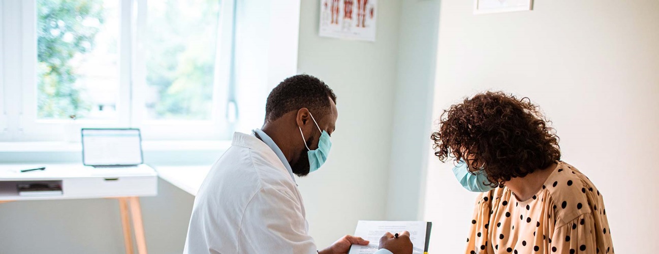 Masked doctor explains procedure to patient in a sunny exam room