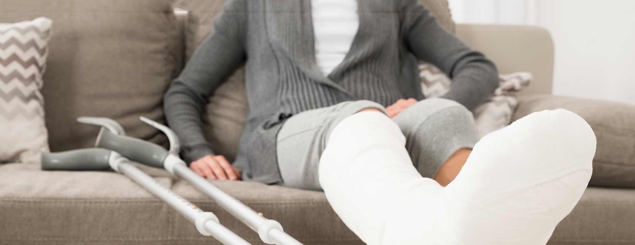 A person elevates their broken leg while sitting on the couch.