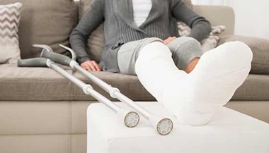 A person elevates their broken leg while sitting on the couch.