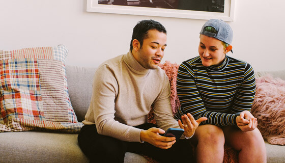 Portrait of trans couple sitting on couch looking at smartphone and talking