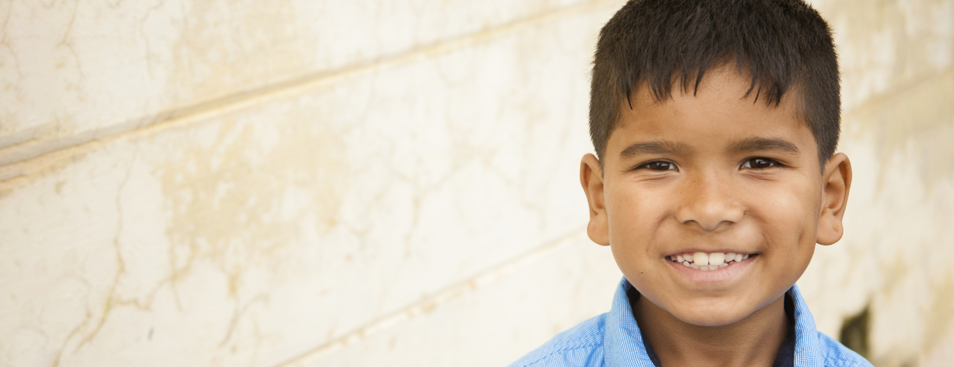 A close up of a little boy smiling in front of a wall.