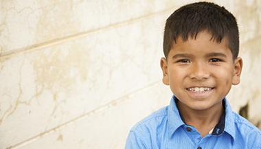 A close up of a little boy smiling in front of a wall.