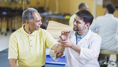 A doctor examines an older male patient's wrist.