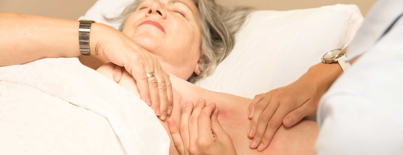 A woman lies down while a lymphedema therapist massages her swollen arm.