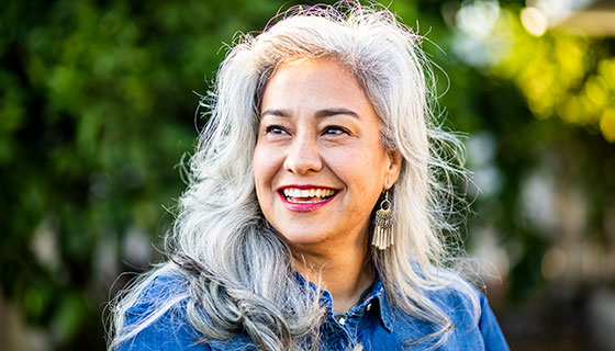 A mature woman stands outside, smiling broadly.