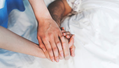 Woman holding a male patients hand while he is in a hospital bed