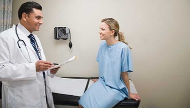 A doctor speaks to a female patient in a hospital exam room.