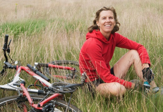 woman sitting in a field next to her bike