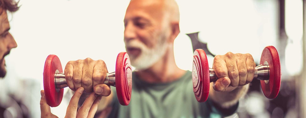Older man in a gym lifting weights in both hands