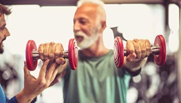 Older man in a gym lifting weights in both hands