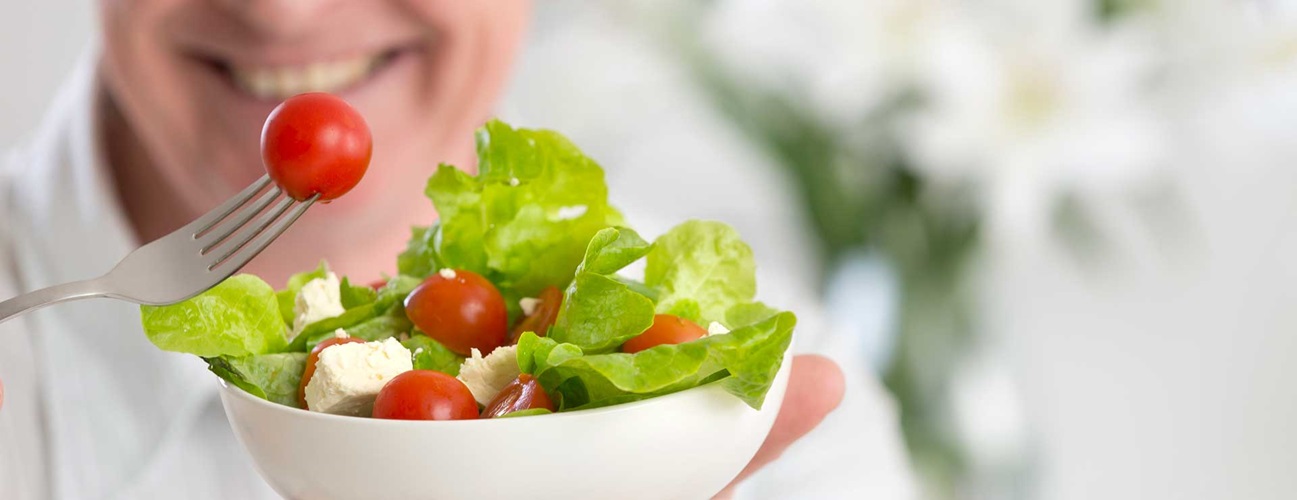 Older man holding a bowl of salad in one hand and a fork with tomato on it in the orther