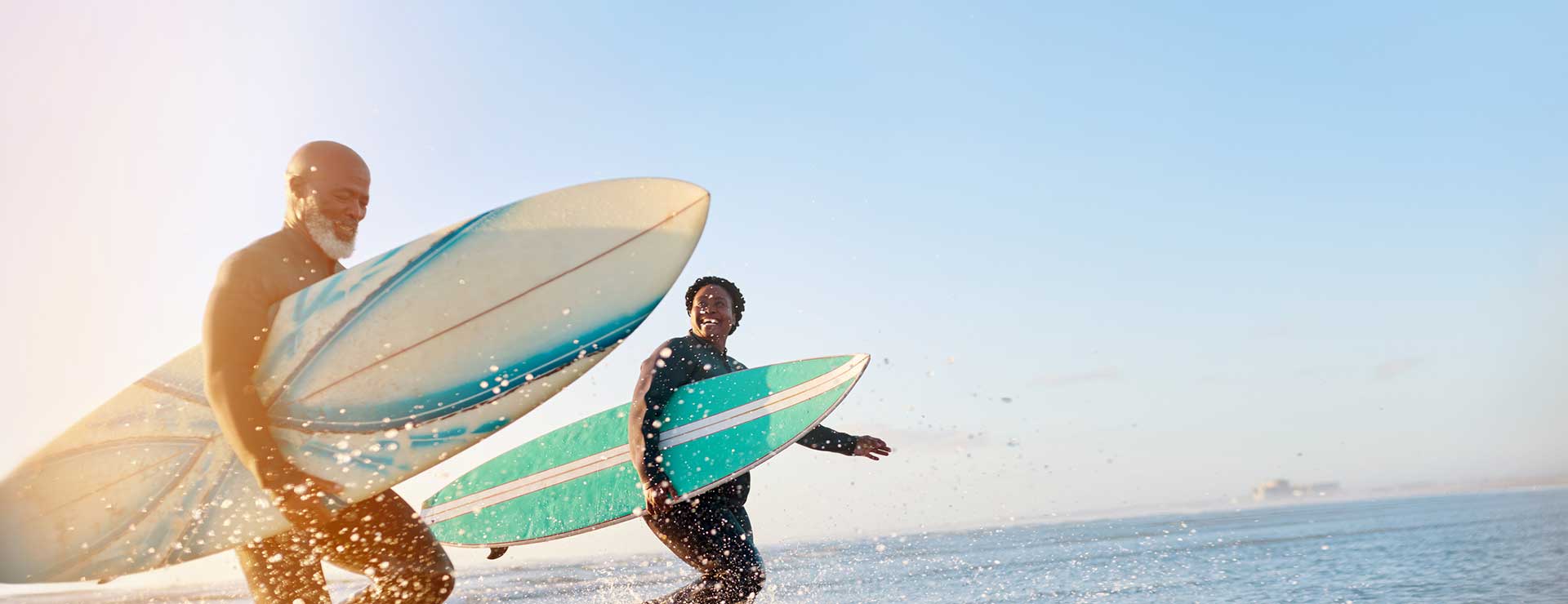 An older couple carrying surf boards out of the ocean