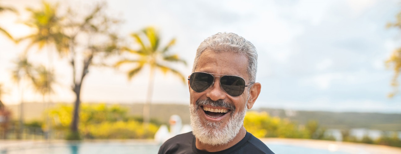 A senior man smiles outdoors while wearing sunglasses
