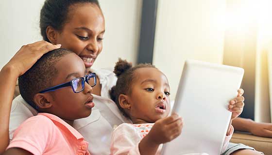 Boy wearing glasses and looking at an iPad with his mother and sister
