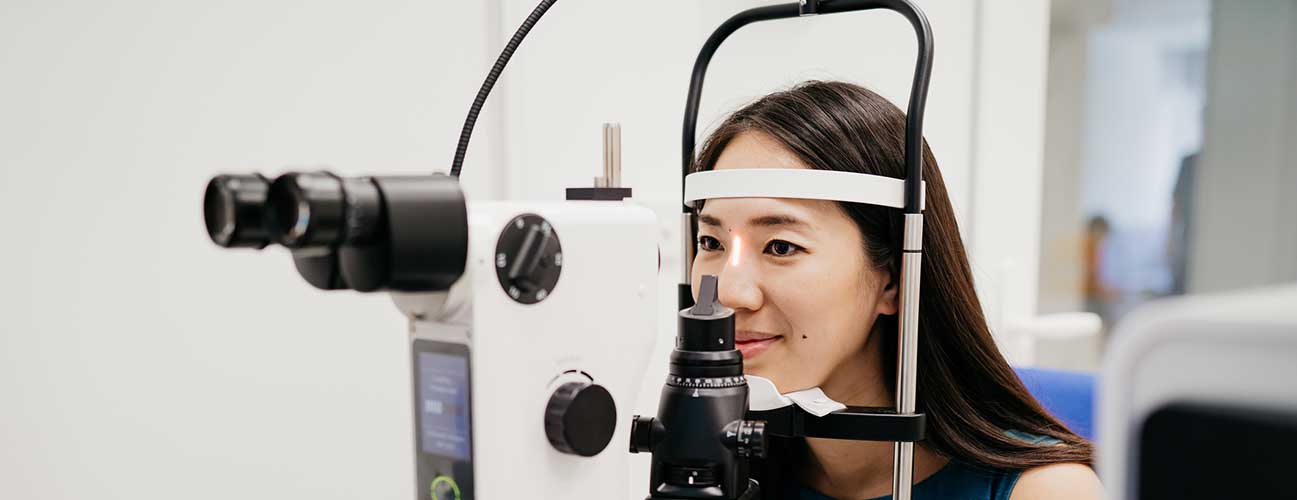 Young woman rests her face in a slit lamp