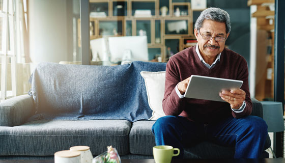 A senior man with glasses using his mobile tablet on the couch