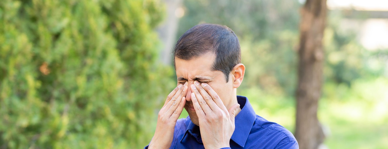 a man outdoors rubbing his eyes
