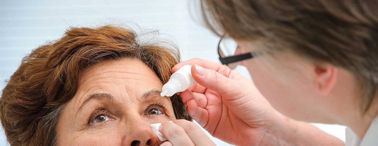 A senior woman receives eye drops from doctor