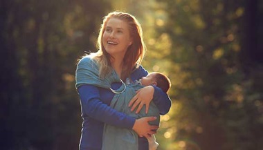 Happy woman carrying a baby outdoors
