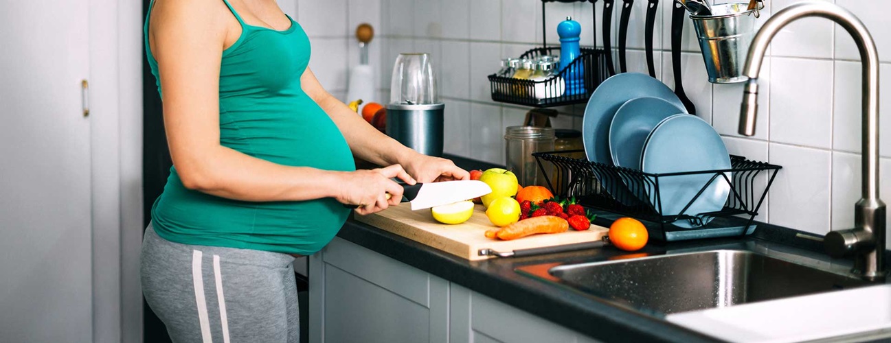 A pregnant woman cuts fruit for a smoothie.
