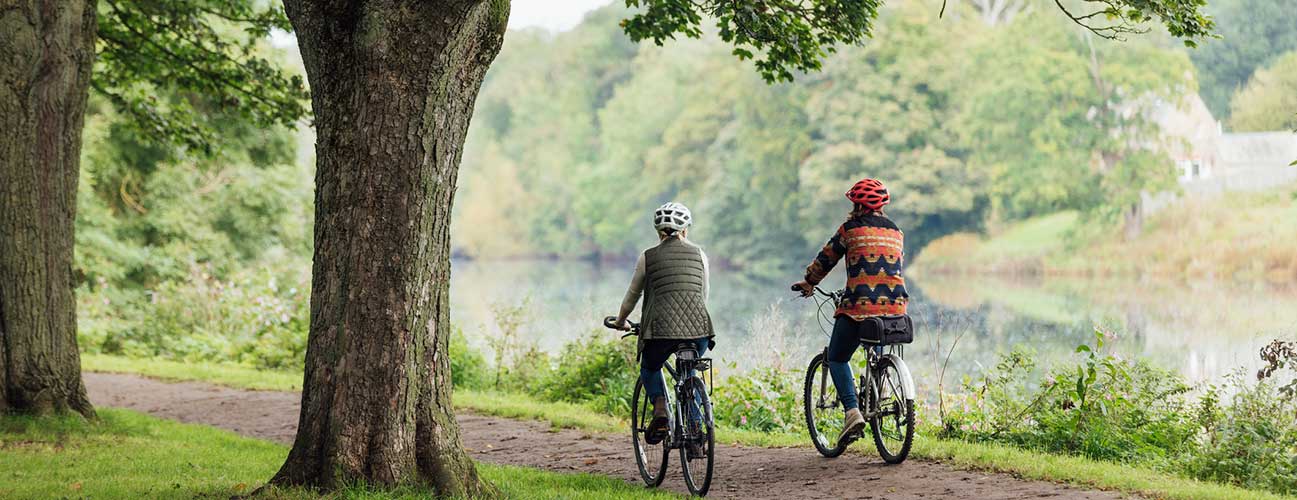 A couple bikes leisurely along a lush, lakeside path
