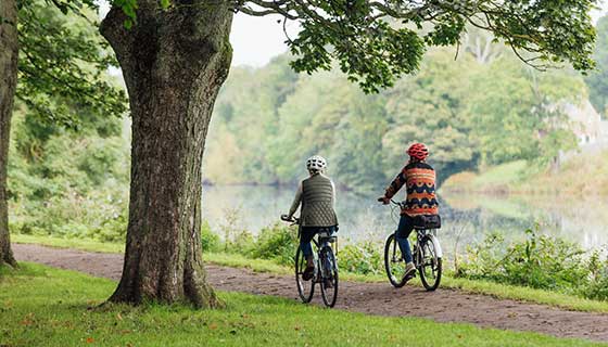 A couple bikes leisurely along a lush, lakeside path