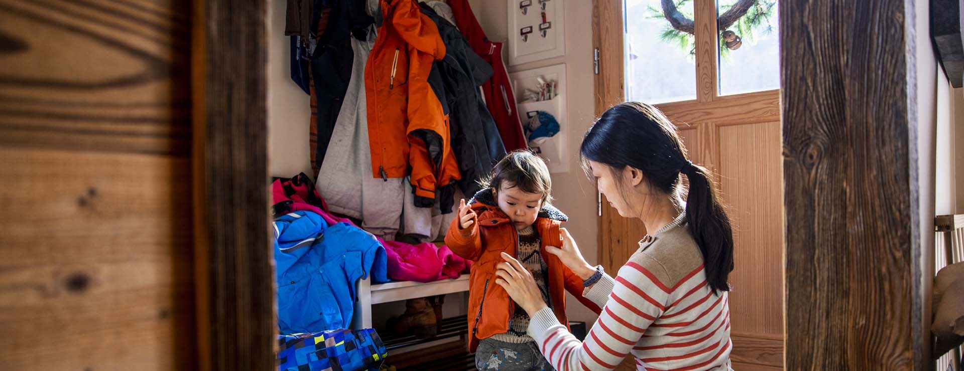 Mom helping daughter with winter jacket in mudroom