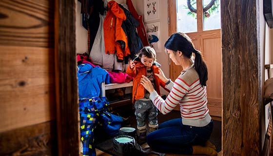 Mom helping daughter with winter jacket in mudroom