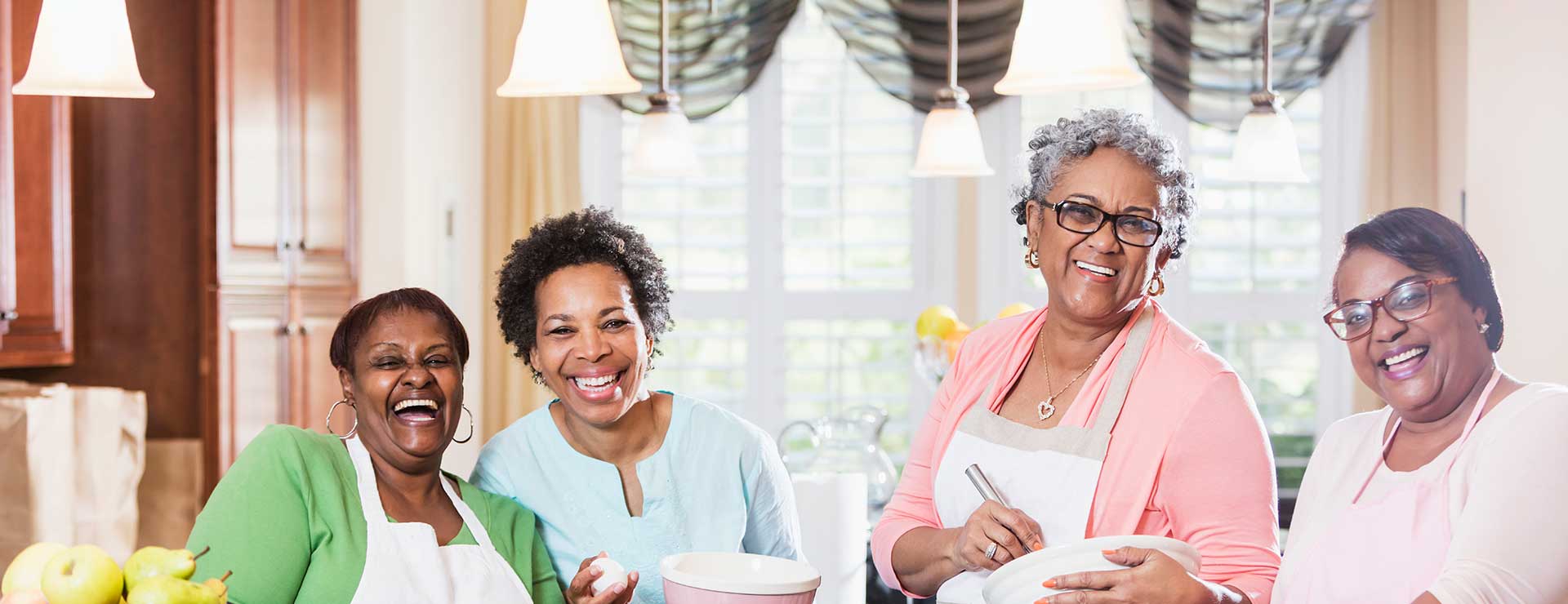 A group of women laugh together in the kitchen.