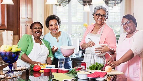 A group of women laugh together as they cook holiday dinner.
