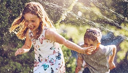 A boy chasing a girl through water spray in play