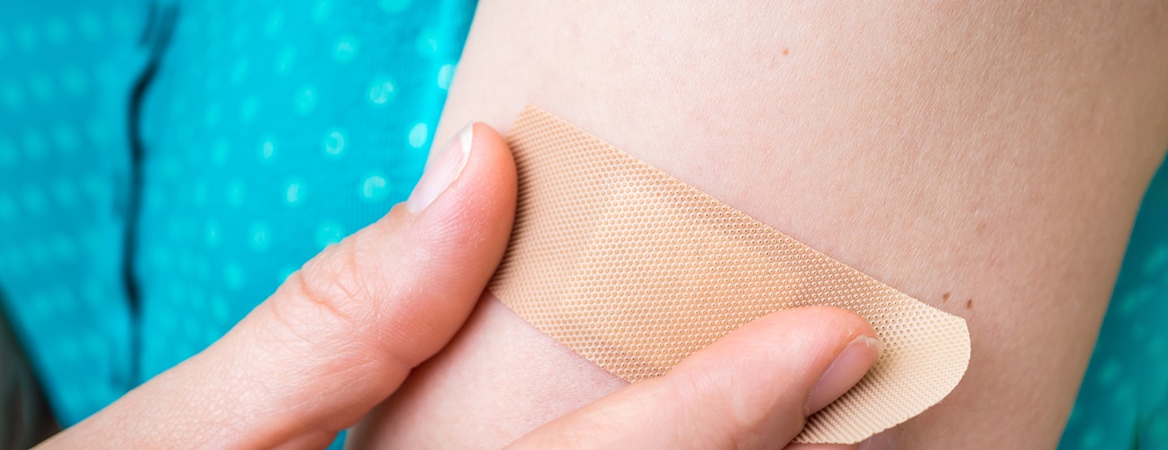 A woman applies a band-aid to her arm.