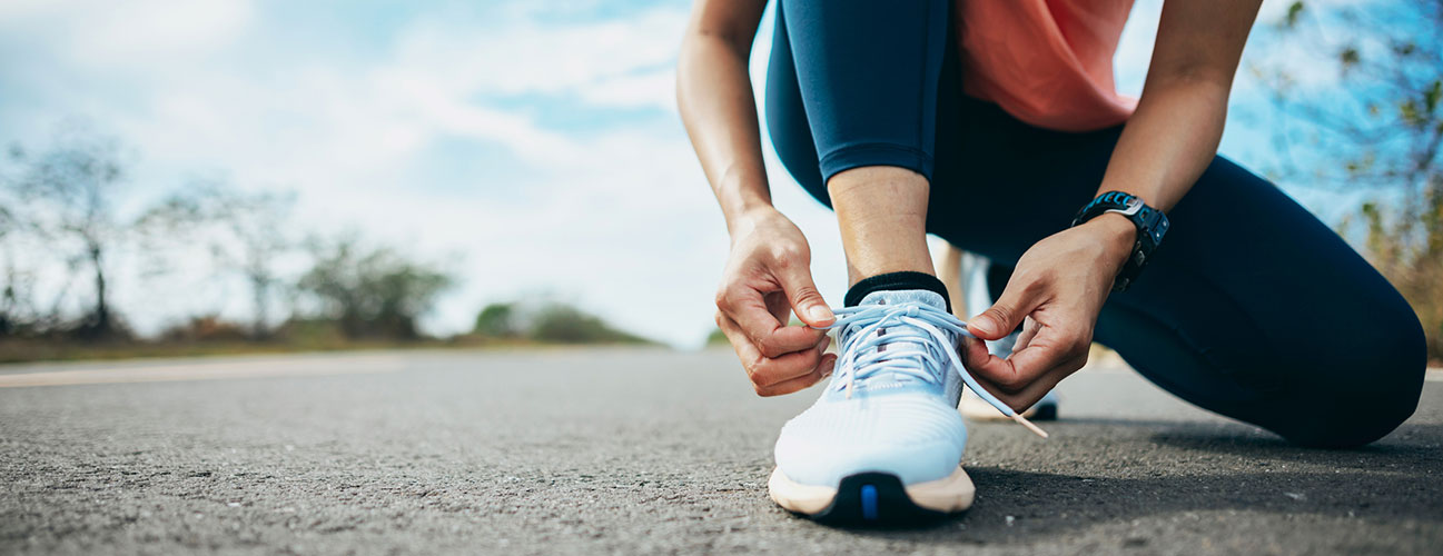 Woman laces her running shoes on a sunny morning