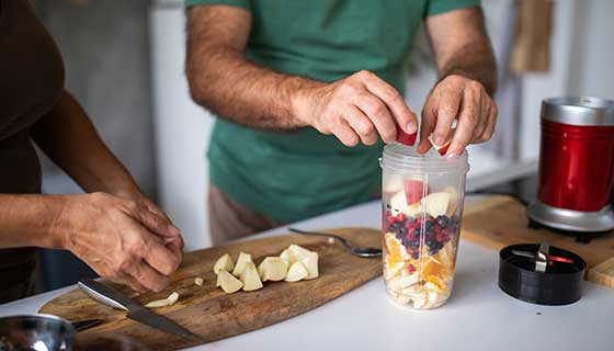 Two adults chop fresh fruit to blend a smoothie
