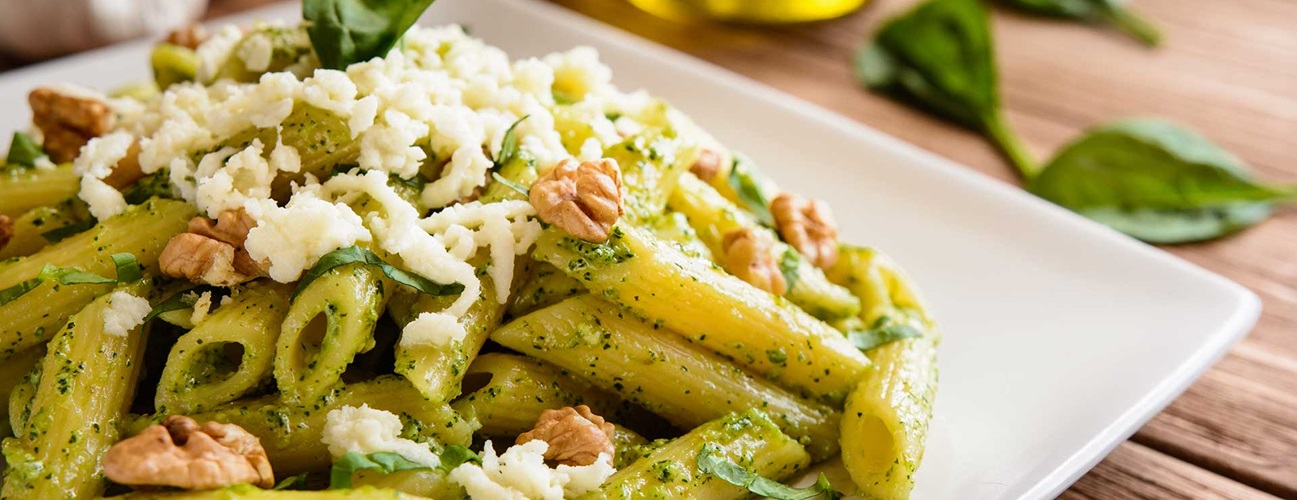A plate of pesto pasta topped with cheese and walnuts.