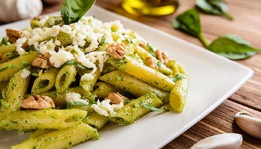 A plate of pesto pasta topped with cheese and walnuts.