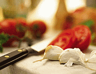 Tomatoes and garlic on a cutting board. Knife sitting next to the ingredients.
