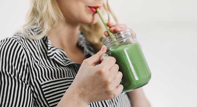 A woman drinks a green smoothie with a straw.