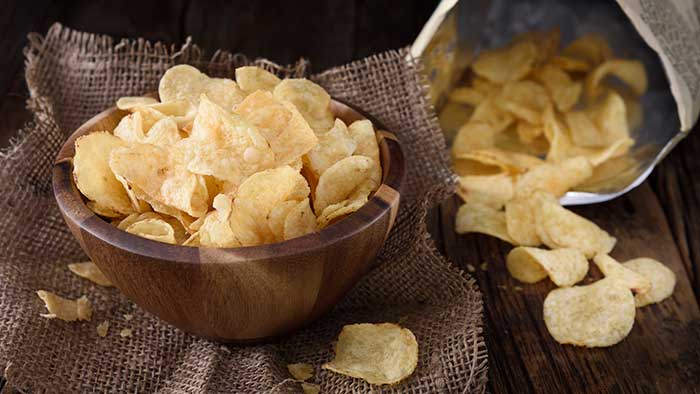 A bowl of potato chips with an opened bag sitting behind