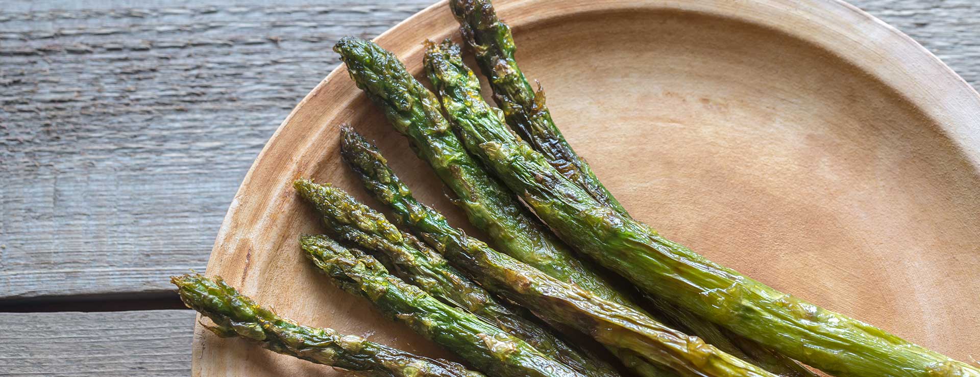 Roasted asparagus on a wooden plate.