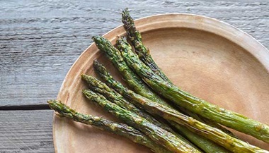 Roasted asparagus on a wooden plate.