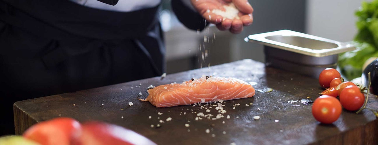 a chef seasons a fresh salmon filet