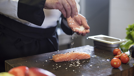 a chef seasons a fresh salmon filet