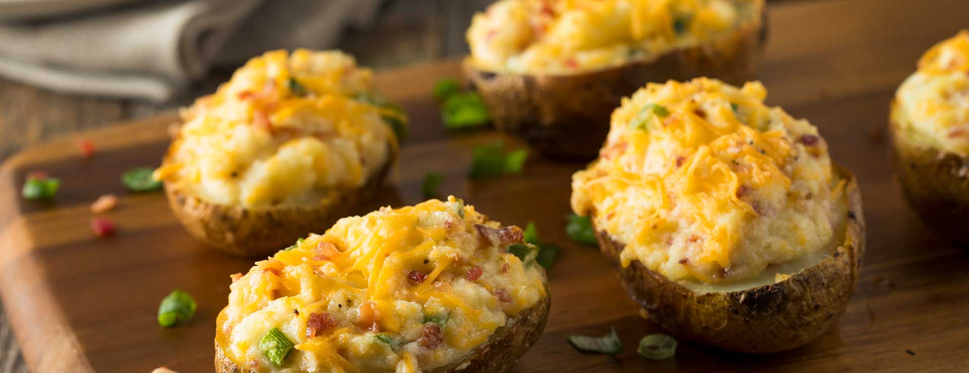 Four baked potatoes on a cutting board.
